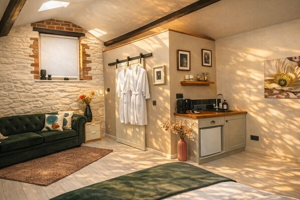 Une pièce chaleureuse avec un mur en pierre, un canapé vert, un banc en bois, une petite kitchenette et une fenêtre.