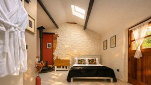 Une chambre avec un mur en pierre, un lit recouvert d’une couverture noire, un banc en bois et un mur rouge.