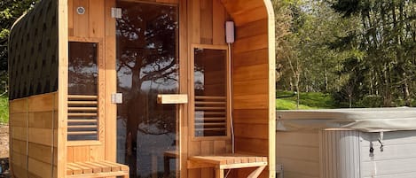 Un sauna en bois avec une porte en verre, un petit banc en bois et un jacuzzi.