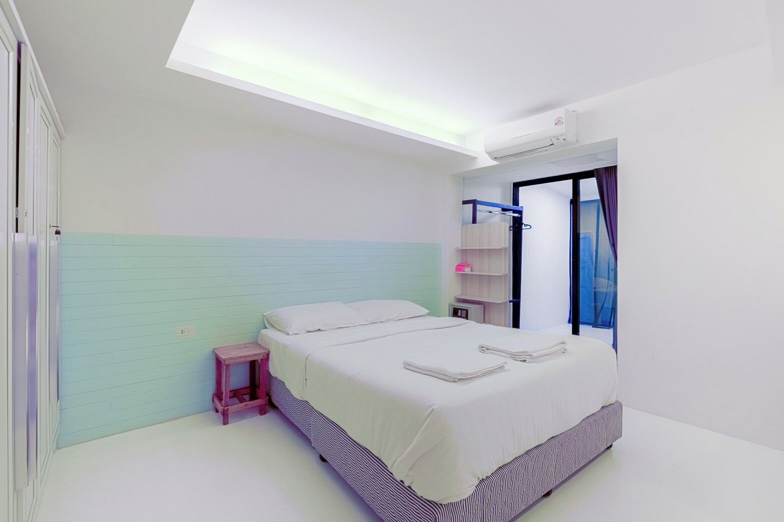A modern bedroom with a bed, bedside table, and a small stool.