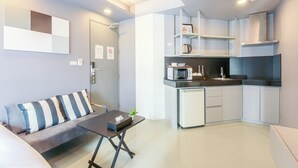 Een knus leefruimte met een kitchenette, een bank met gestreepte kussens, een klein tafeltje en een plant in pot.