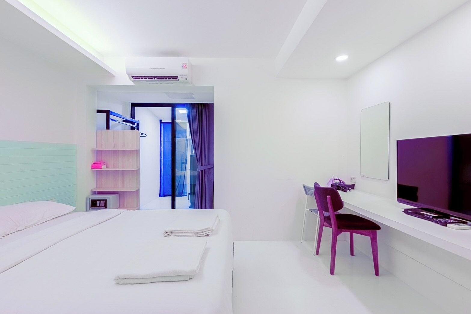 A modern hotel room with a bed, a desk with a chair, a TV, and a window with curtains.