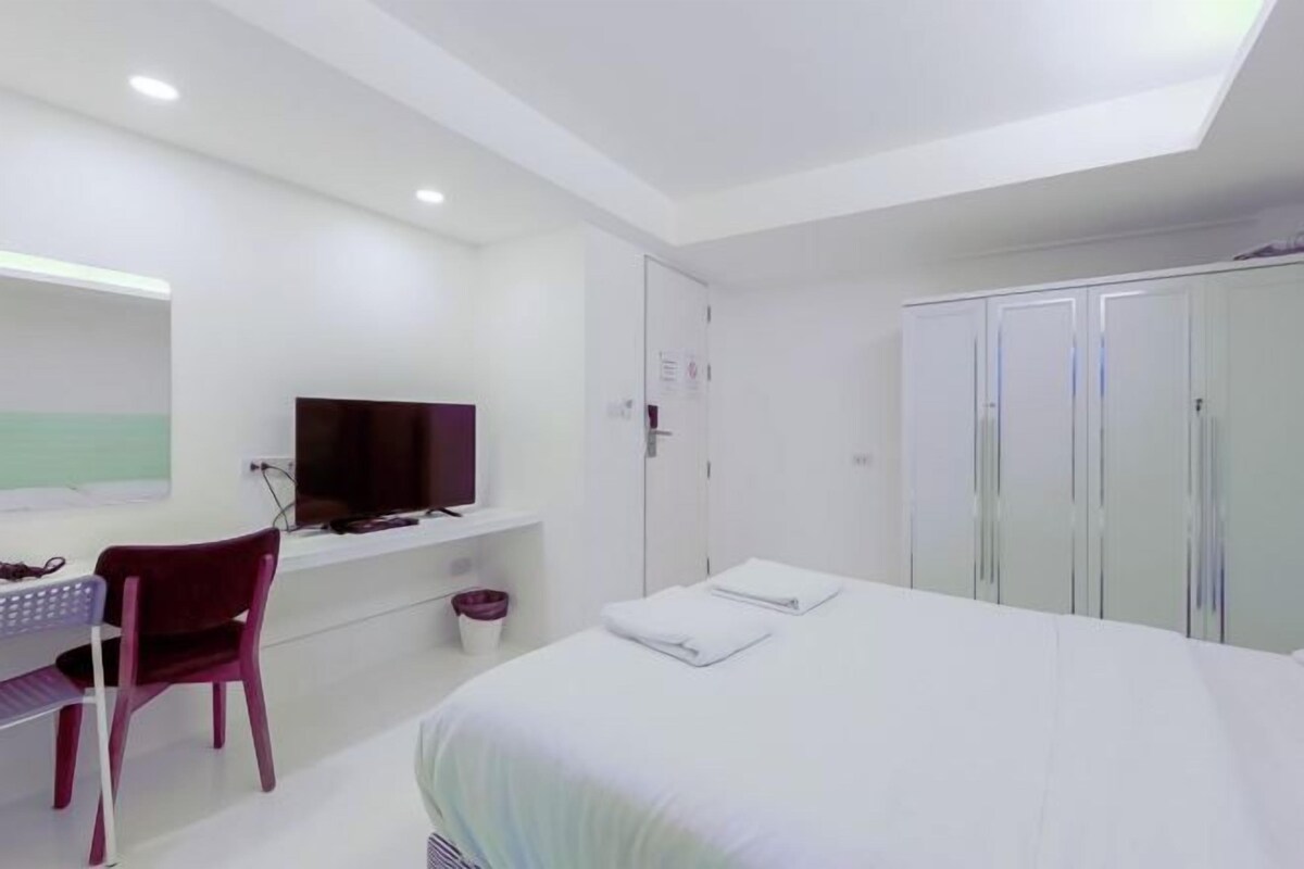 A modern hotel room with a bed, a desk, a chair, a television, and a wardrobe.