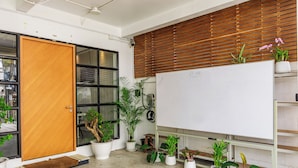 Een kamer met een whiteboard, een houten deur, planten in potten en een betonnen vloer.