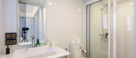 A modern bathroom with a white sink, toilet, and glass shower enclosure.