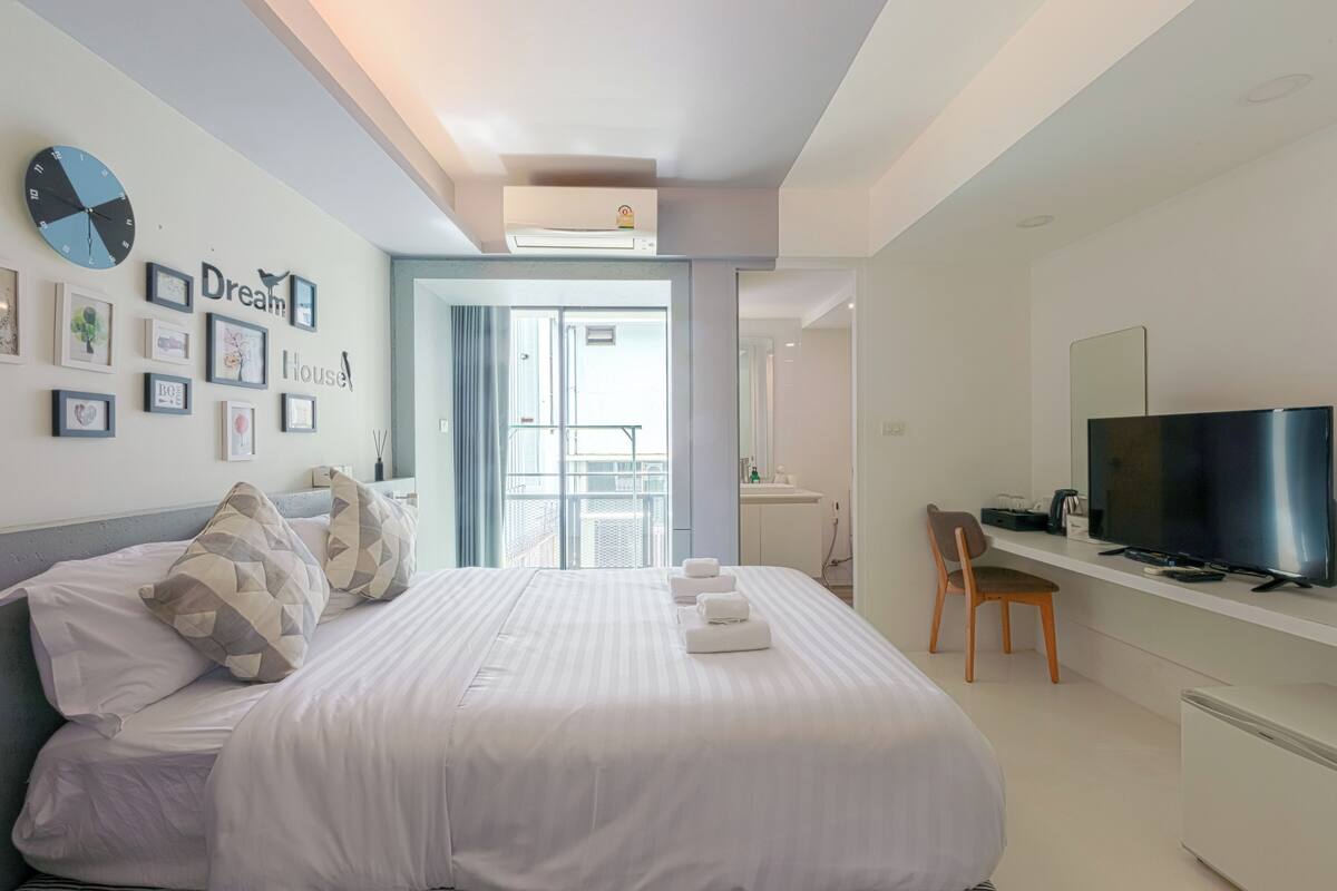 Moderni hotellihuone, jossa on sänky, televisio, työpöytä ja parveke.