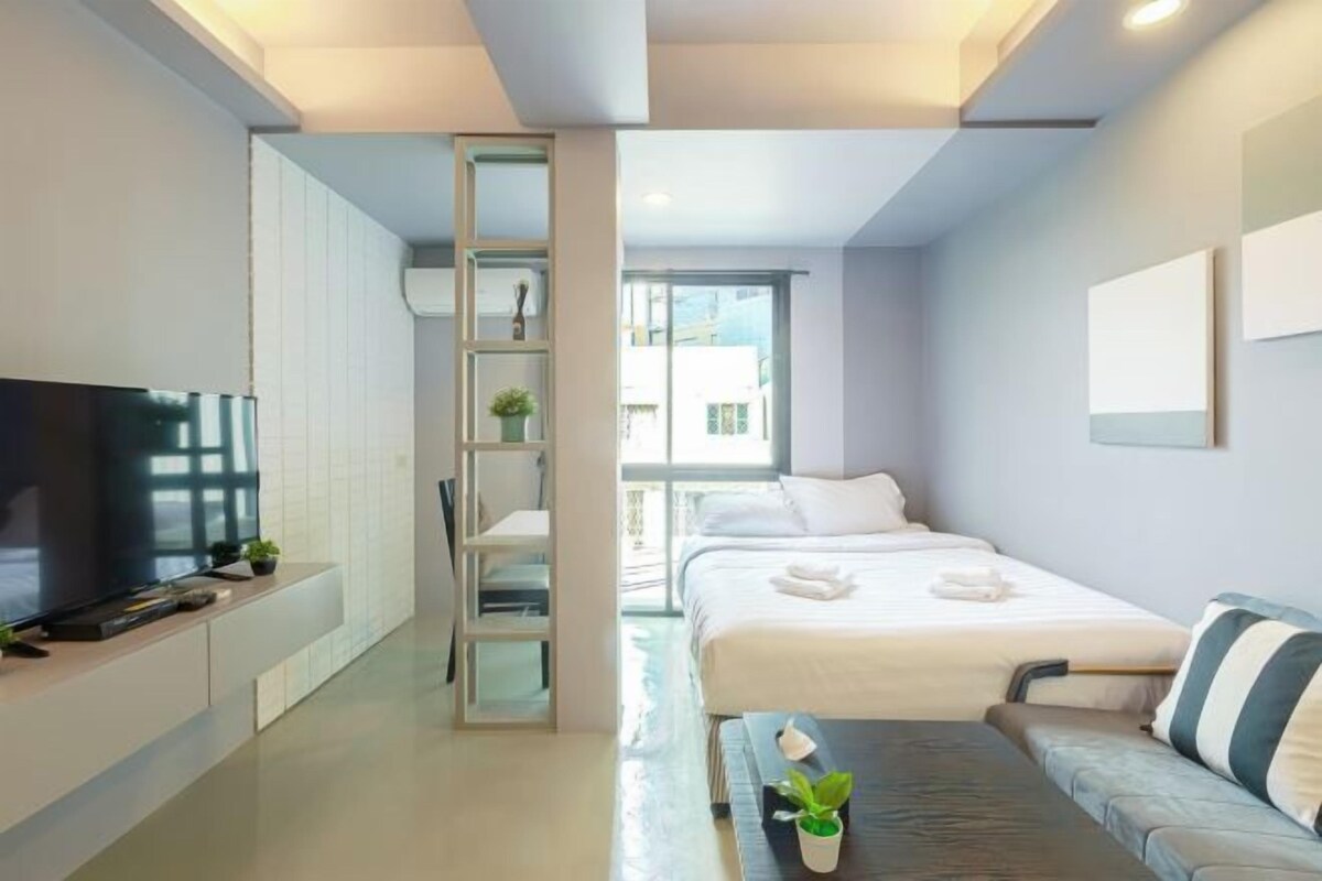 A modern hotel room with a bed, a sofa, a TV, and a small table with a plant.