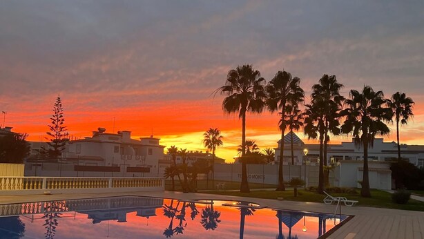 A swimming pool with a clear reflection, surrounded by palm trees and buildings during sunset. - Apartment O Monte with pool and tennis court  (Guia)