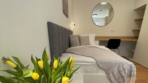 Een moderne slaapkamer met een bed, een nachtkastje met een vaas gele tulpen, een ronde spiegel aan de muur en een houten vloer.