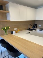 Una cocina moderna con armarios blancos, encimera de madera, cafetera y un florero con flores amarillas.
