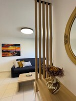 Una sala de estar moderna con un sofá oscuro, una mesa de centro, un jarrón con flores secas, un cuadro de un atardecer y un espejo decorativo.