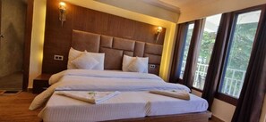 A double bed with a headboard, bedside lamps, and a view of greenery through large windows. - Hotel Taj palace Dalhousie (Dalhousie)