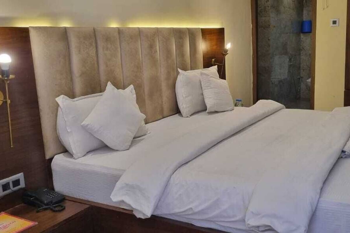A hotel room with a large bed, a wooden headboard, a bedside table with a lamp, and a wardrobe.