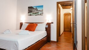 A hotel room with a bed, a wooden headboard, a wall-mounted picture, and a hallway leading to another room. - Domus Lxvii Monti in Rome (Rome)
