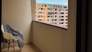A balcony with a view of a multi-story building, a chair with a blanket, and a tiled floor. - Welcome Malibu Apartments (Yerevan)