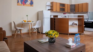 A compact living space with a kitchenette, a dining area, and a small table with a vase of flowers and a tissue box. - Welcome Malibu Apartments (Yerevan)