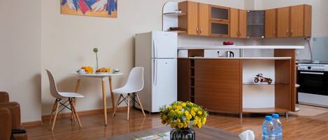 A compact living space with a kitchenette, a dining area, and a small table with a vase of flowers and a tissue box.