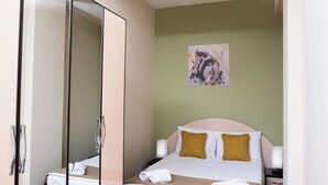 A neatly made bed with white and mustard pillows, a bedside table with a lamp, and a painting on the wall. - Welcome Malibu Apartments (Yerevan)