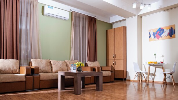 A modern living room with a sofa, coffee table, and a dining area with chairs and a table. - Welcome Malibu Apartments (Yerevan)