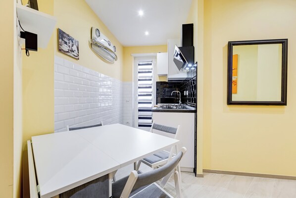 A compact kitchen with white cabinets, a white tiled backsplash, and a small dining area with a white table and grey chairs. - Monteverde Cozy Apartment (Rome)