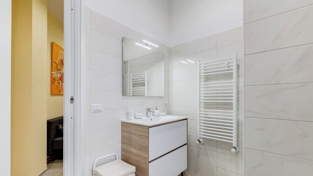 A modern bathroom with a white vanity, a mirror, a towel rack, and a small stool. - Monteverde Cozy Apartment (Rome)