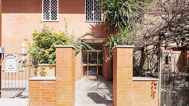 A brick building with a gated entrance, a mailbox, and a small garden area with plants. - Monteverde Cozy Apartment (Rome)