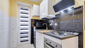 A compact kitchen with white cabinets, a black stove, and a microwave. - Monteverde Cozy Apartment (Rome)
