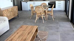 A modern kitchen with white cabinets, a dining area with wicker chairs, a wooden coffee table, and a ceiling fan. - Sunset - Front de mer (Trois-Bassins)