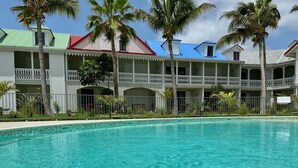 A pool with clear water, surrounded by a building with balconies and palm trees. - Studio Eleven Alamanda Beach beachfront (Saint Martin)
