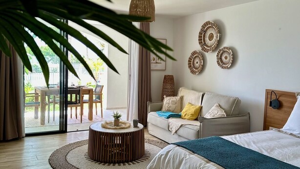 A modern bedroom with a bed, a round wooden coffee table, a sofa, and a dining area with a table and chairs. - Studio Eleven Alamanda Beach beachfront (Saint Martin)