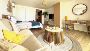 A modern, well-lit room with a sofa, a round wooden coffee table, a TV, a desk, and a mirror. - Studio Eleven Alamanda Beach beachfront (Saint Martin)