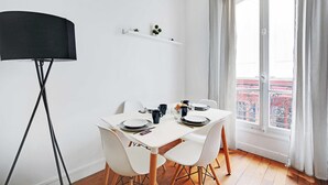 A dining area with a white table set for four, white chairs, a black floor lamp, and a window with curtains. - Cosy 1br/4p - Montmartre/sacre Coeur (Paris)