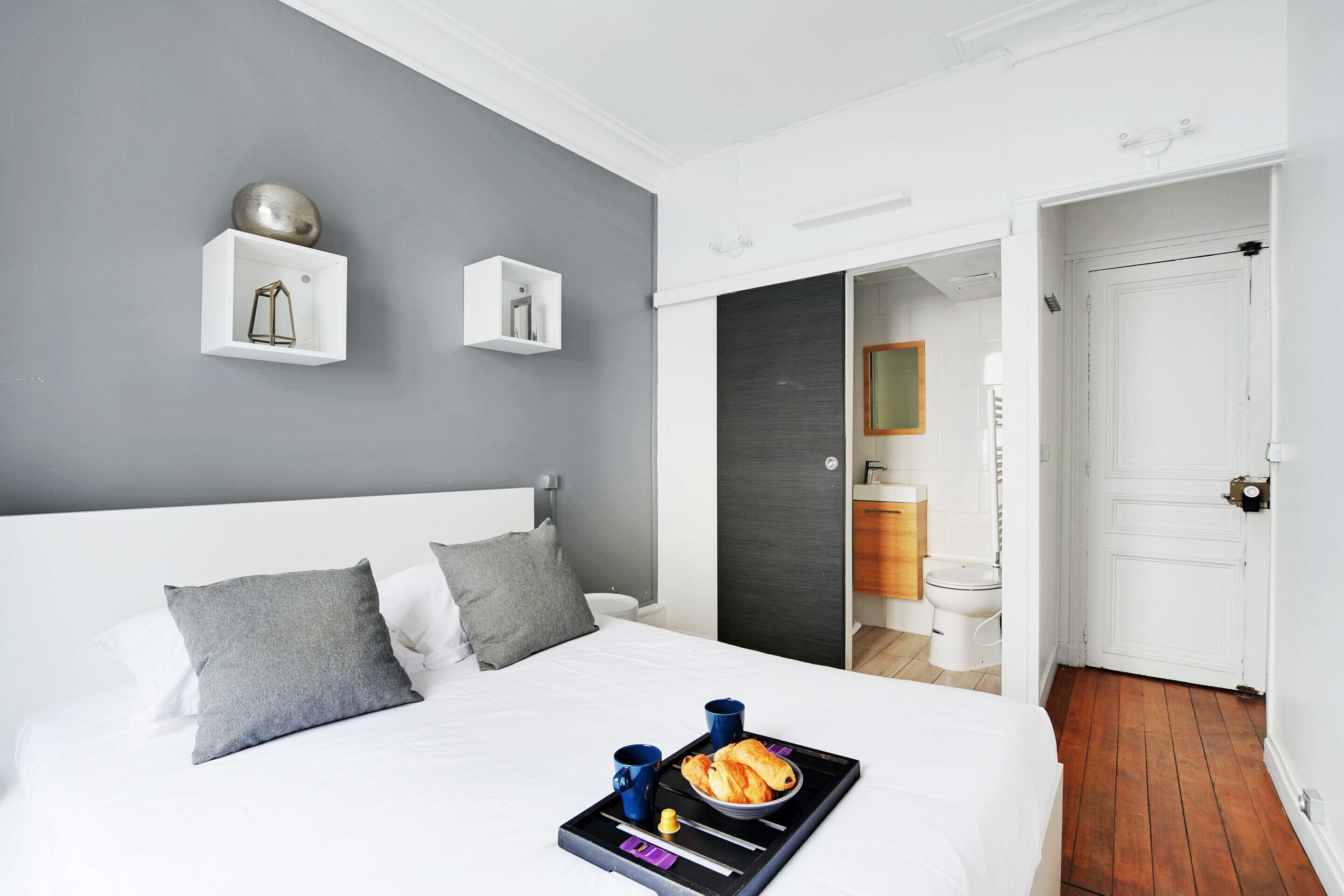 A hotel room with a large bed, grey walls, and a breakfast tray on the bed.