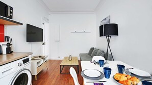 A compact living space with a washing machine, a flat-screen TV, a dining table set with plates, cups, and a plate of croissants. - Cosy 1br/4p - Montmartre/sacre Coeur (Paris)
