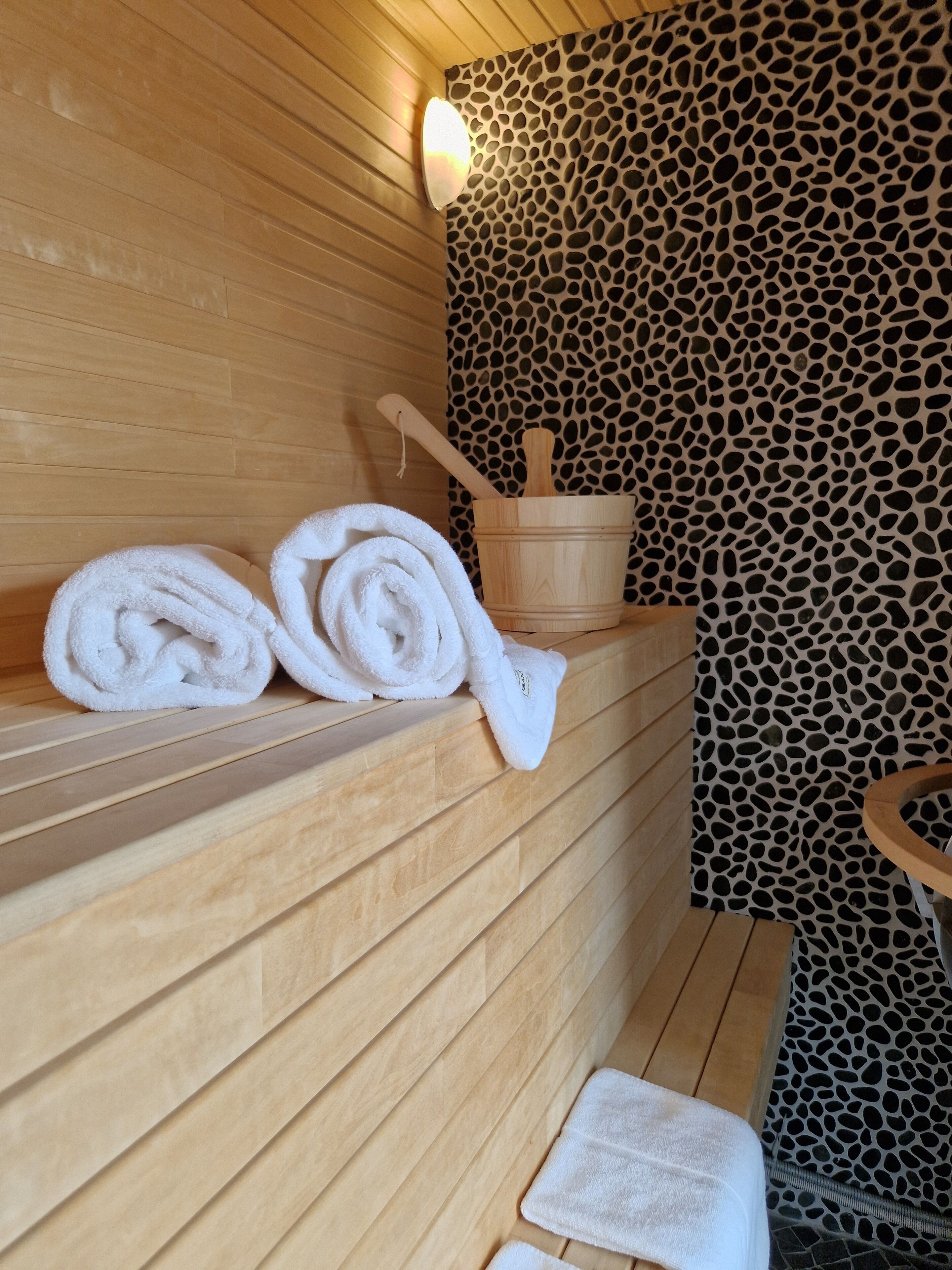 Un banco de madera con toallas y un balde de madera en un entorno de spa.