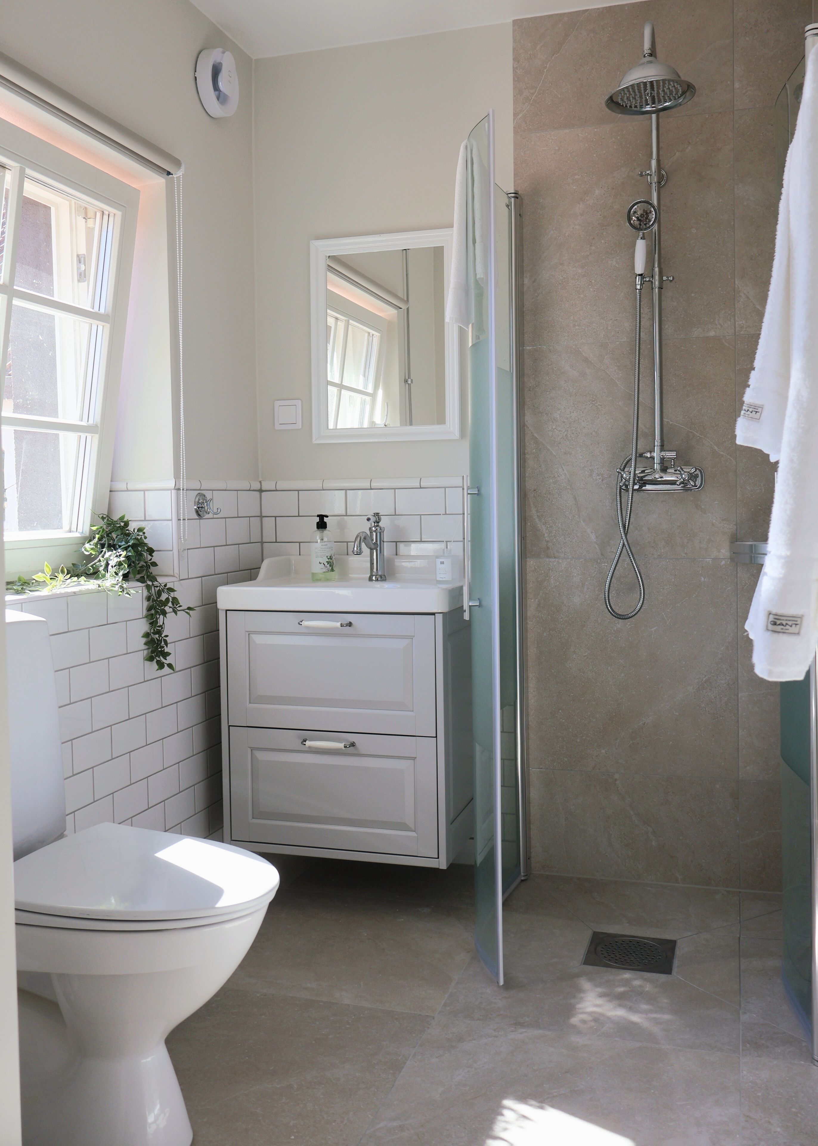 A bathroom with a toilet, a sink with a mirror, a shower with a handheld showerhead, and a towel hanging on the wall.