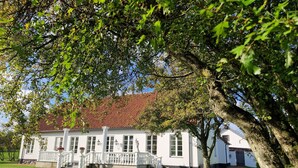 A white building with a red-tiled roof, a white porch, and a well-maintained lawn. - Fontänens Bed & Breakfast (Trelleborg)