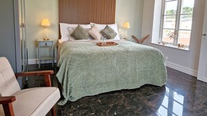 A spacious bedroom with a large bed, a nightstand, a chair, and a window with a view. - Fontänens Bed & Breakfast (Trelleborg)