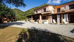A two-story building with a gravel driveway, outdoor seating area, and potted plants. - Vacation home Cartuceddu 3b - Marina di Tertenia (TERTENIA)