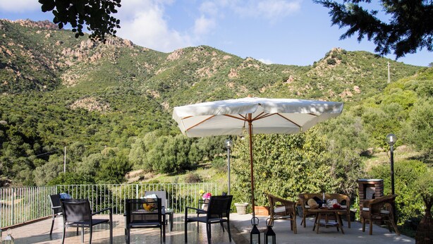 An outdoor patio with chairs and an umbrella, surrounded by a metal fence and overlooking a mountainous landscape. - Vacation home Cartuceddu 3b - Marina di Tertenia (TERTENIA)