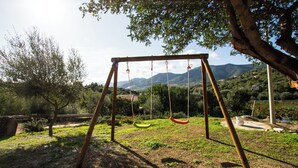 A wooden swing set in a grassy area with trees and mountains in the background. - Vacation home Cartuceddu 3b - Marina di Tertenia (TERTENIA)