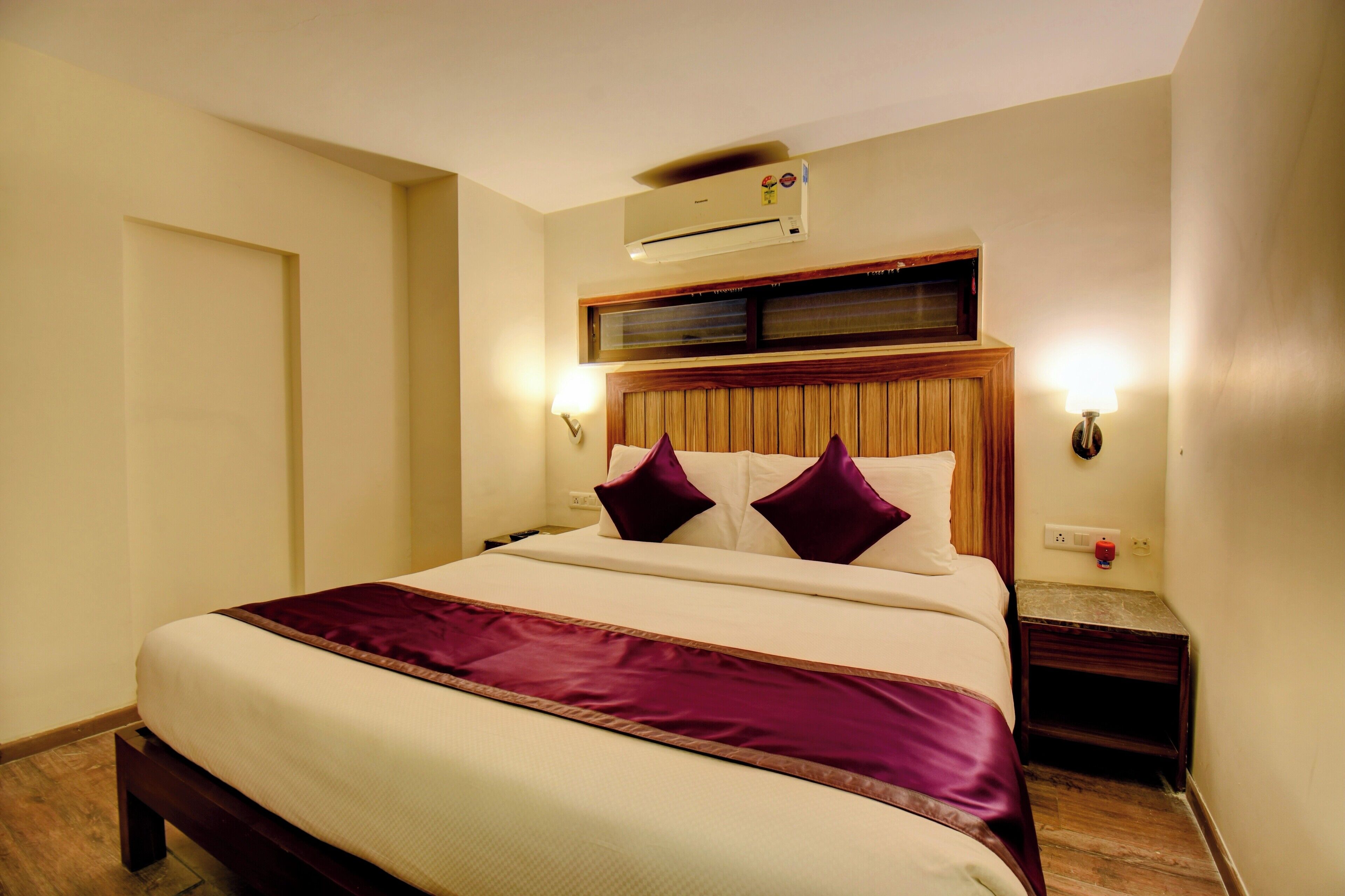 Ein Hotelzimmer mit Bett, Klimaanlage, Nachttisch und Wandlampe.
