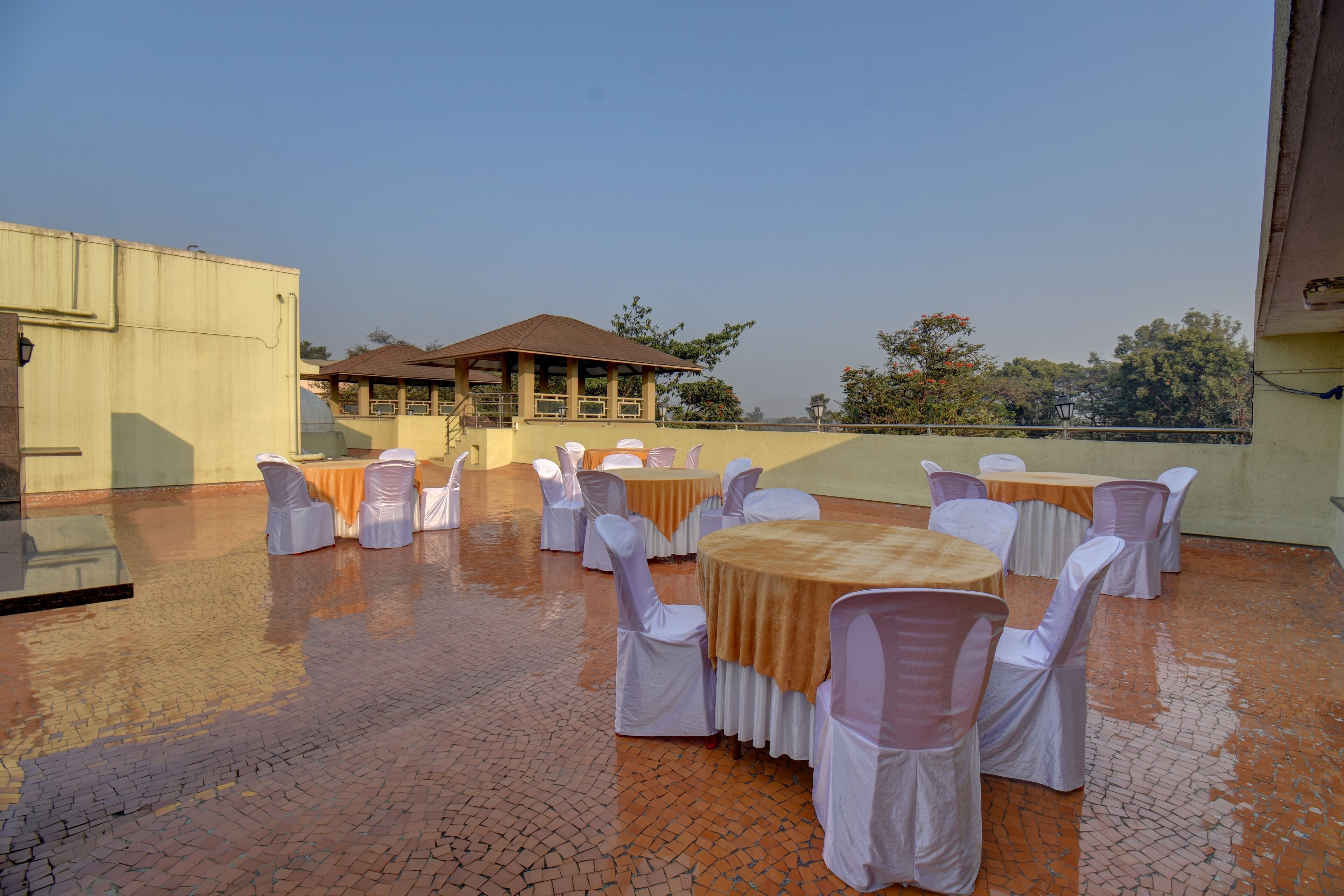 An outdoor patio with round tables and chairs, a covered seating area, and a brick floor.