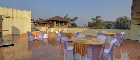 An outdoor patio with round tables and chairs, a covered seating area, and a brick floor.