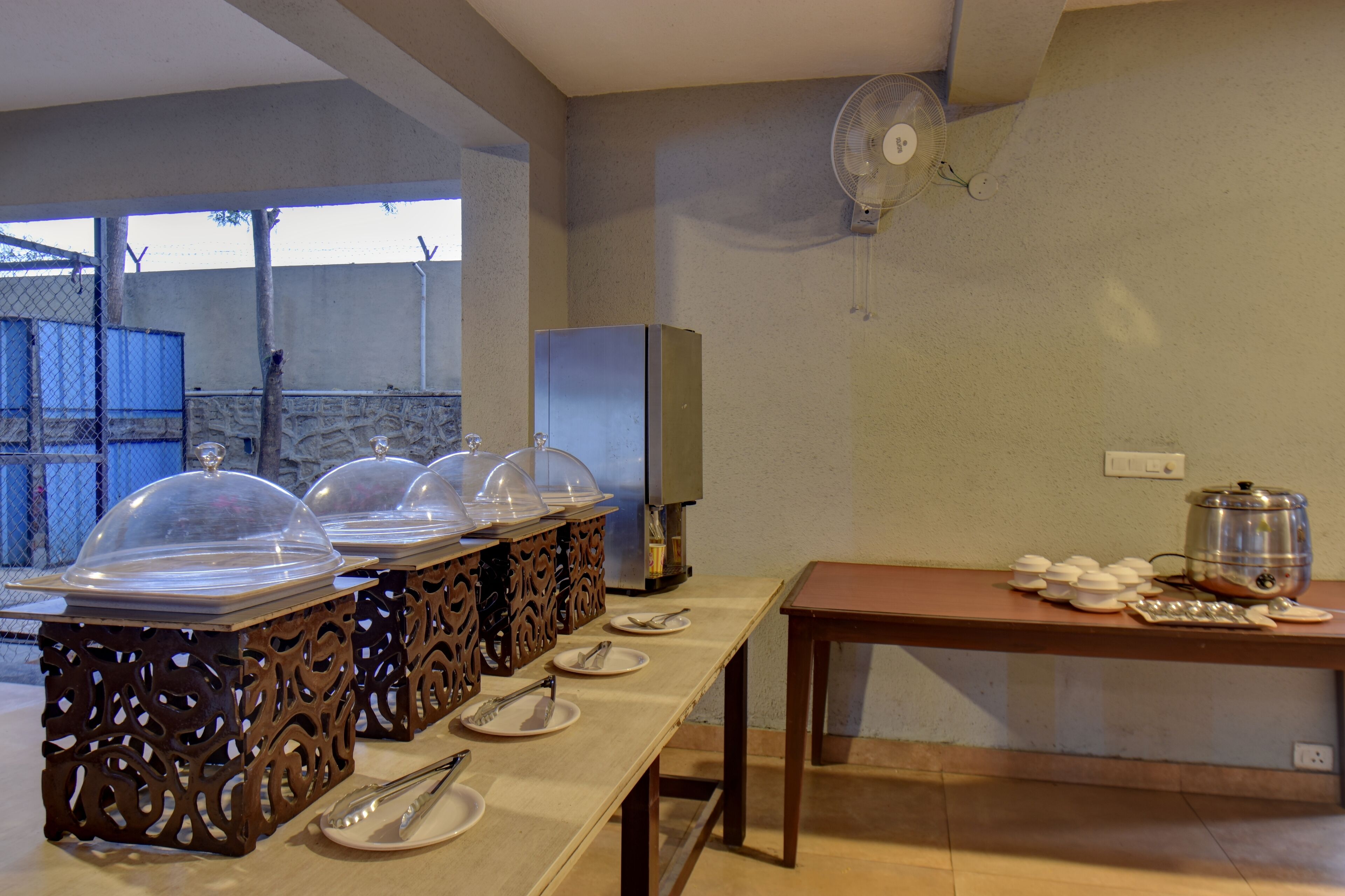 Montaje de bufé con estaciones de servicio cubiertas, un ventilador y una mesa con platos y una olla.