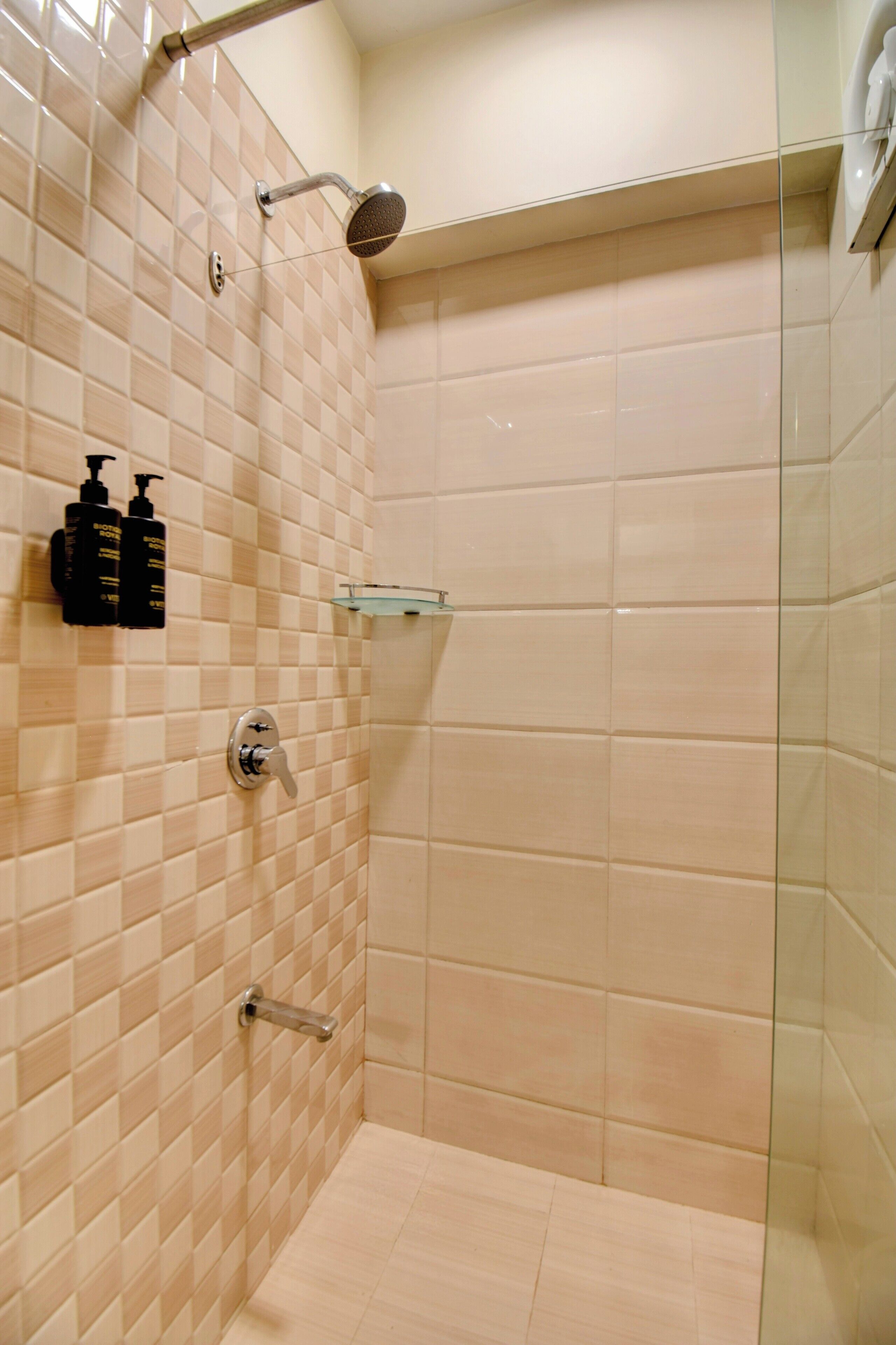 Une douche avec une porte en verre, un sèche-mains et deux bouteilles de shampoing fixées au mur.