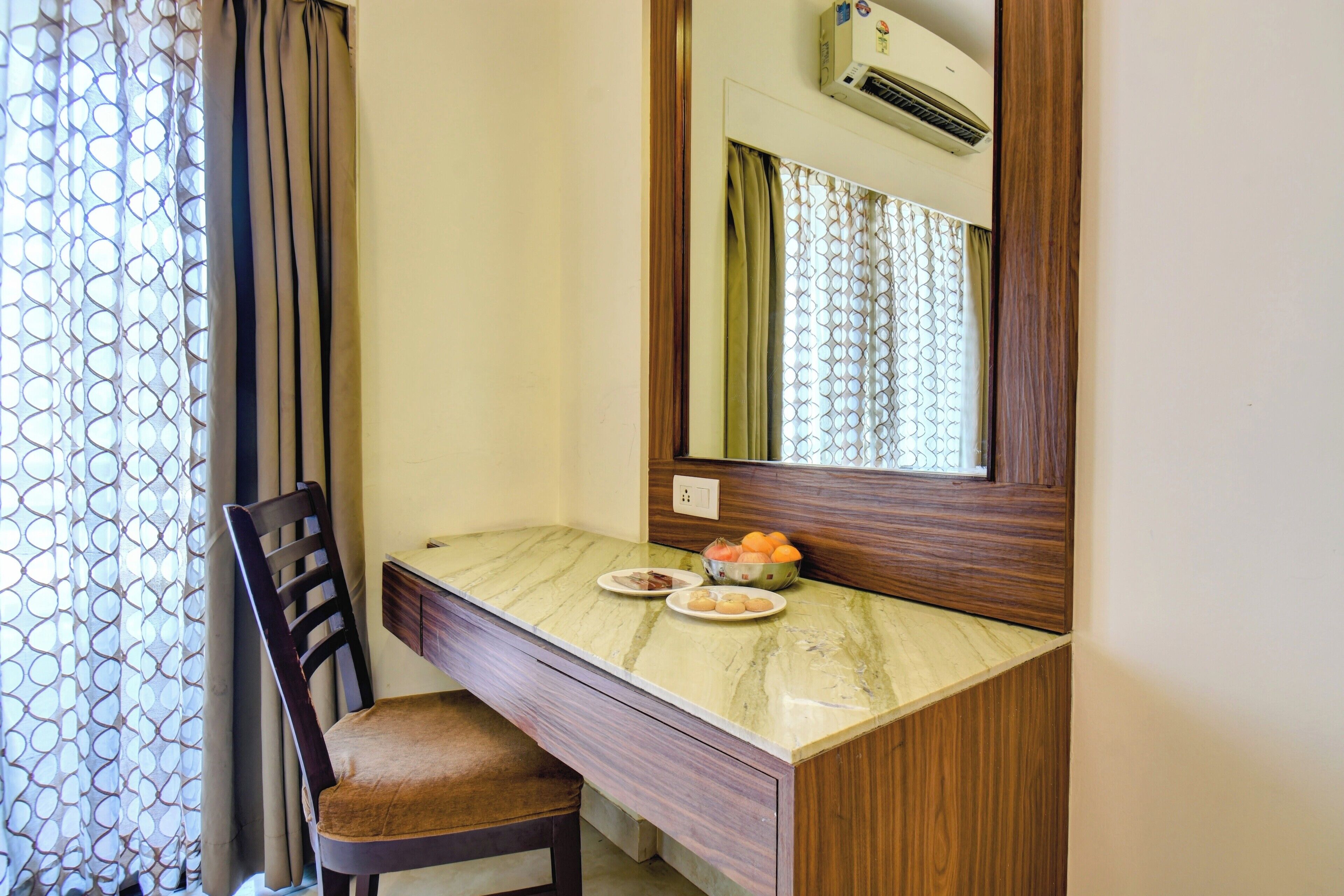A small, private room with a wooden desk, a chair, a mirror, and a bowl of fruit on the desk.