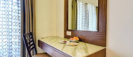 Una habitación pequeña y privada con un escritorio de madera, una silla, un espejo y un frutero sobre el escritorio.