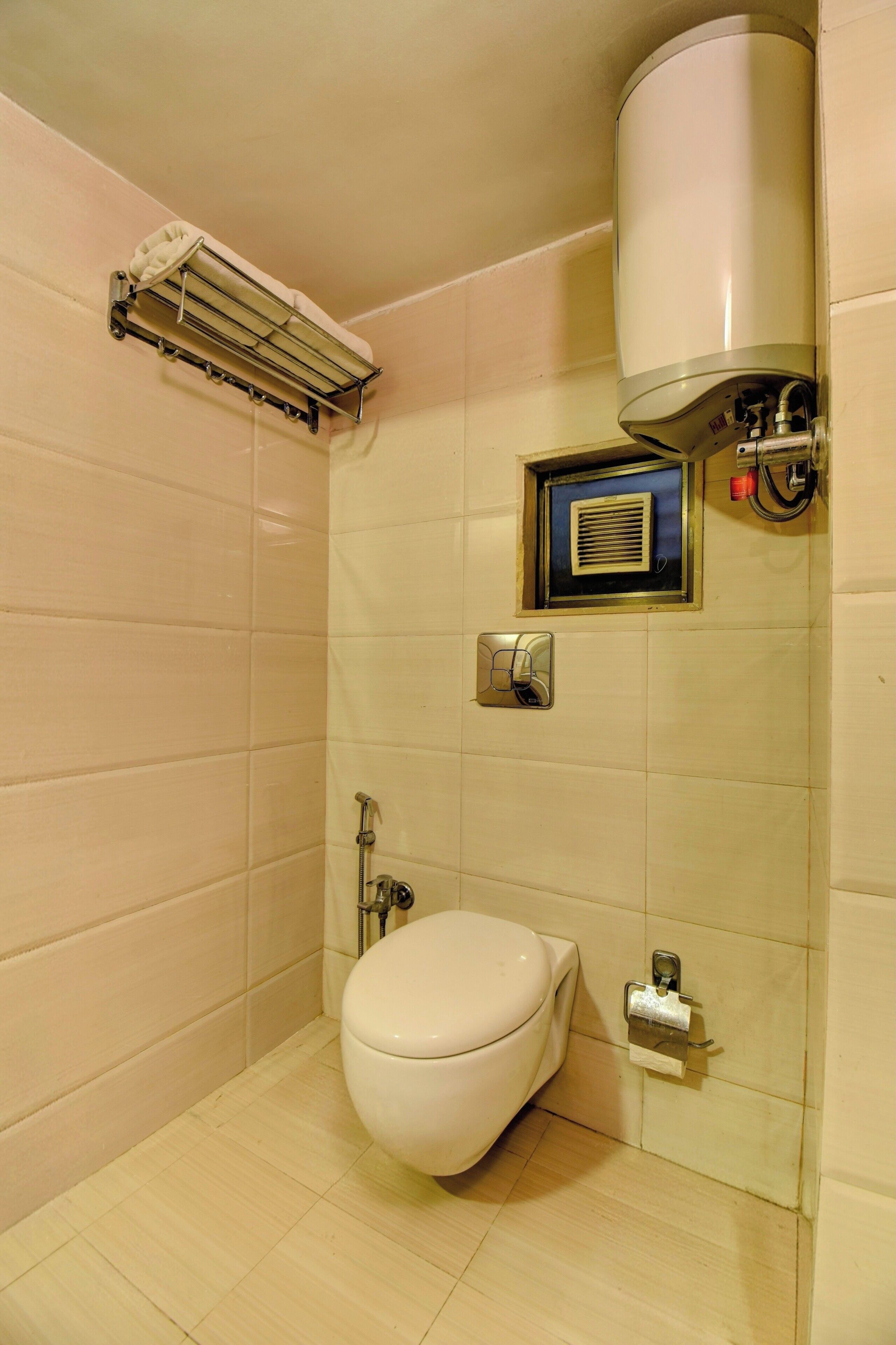 A small, clean bathroom with a toilet, a towel rack, a hand dryer, and a ventilation unit.