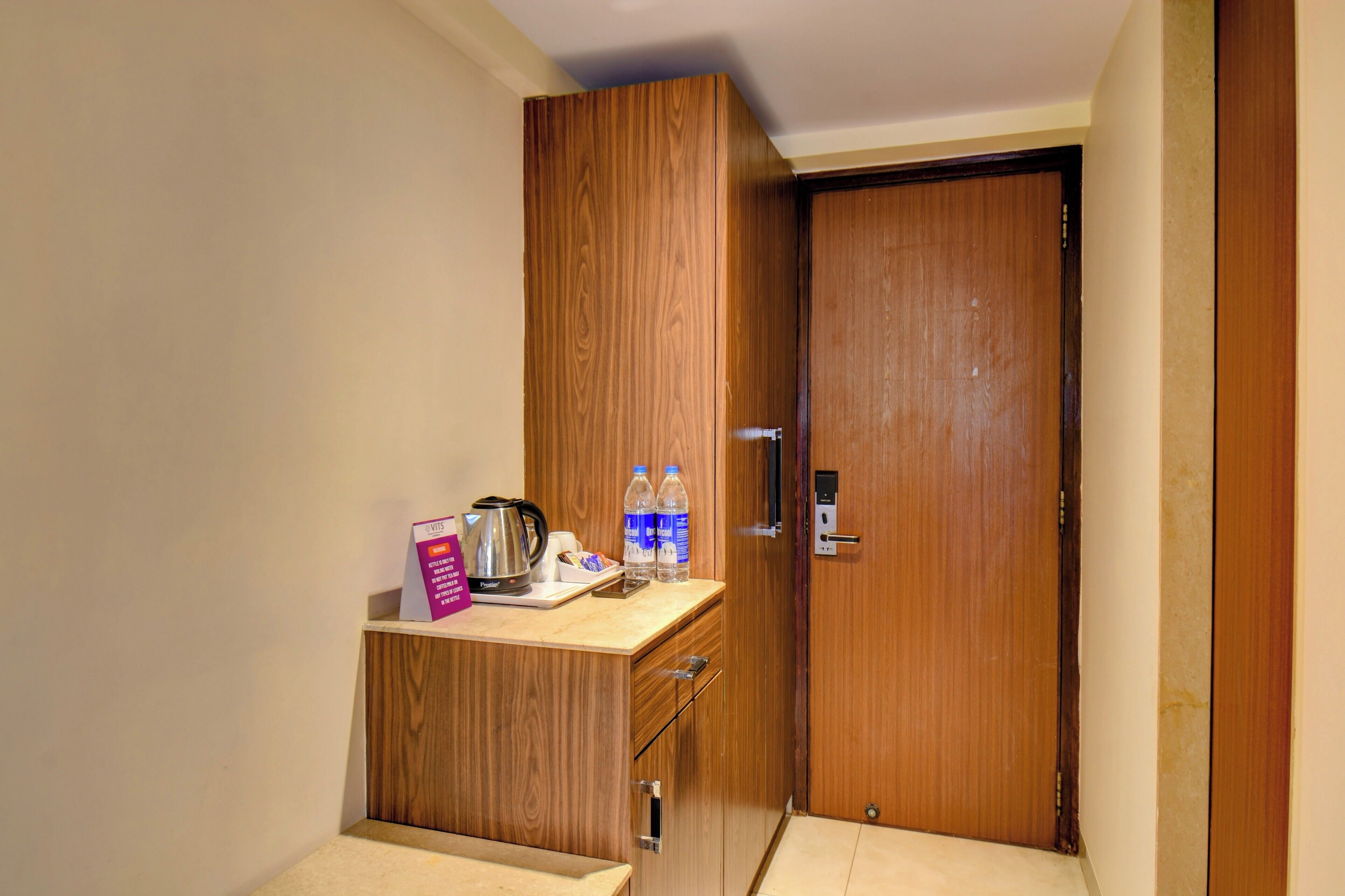 A compact kitchenette with a wooden cabinet, a coffee maker, bottled water, and a box of tissues.